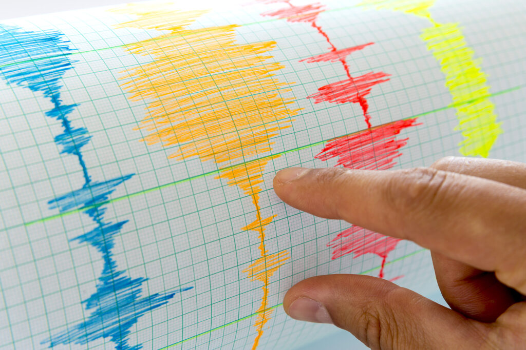 Seismological device for measuring earthquakes. Seismological activity live on the sheet of measuring paper. Earthquake wave on graph paper. Human hand showing earthquake.